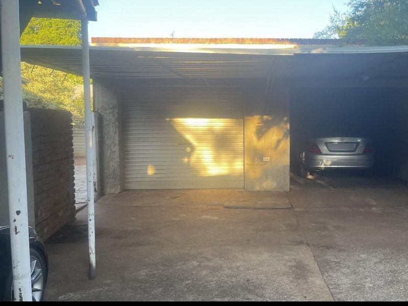 A functional garage area featuring a roller shutter door, concrete driveway, and a covered carport structure.