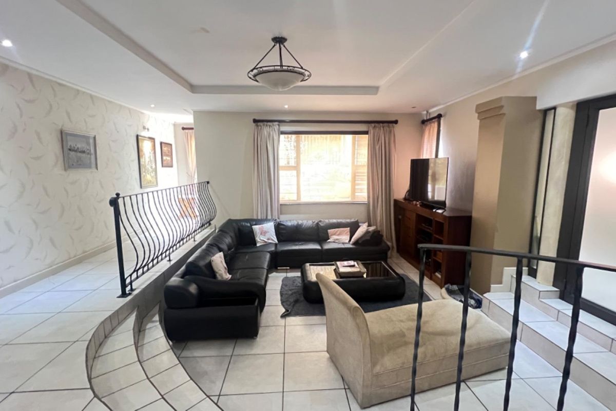 Spacious living room featuring tiled flooring, a sunken seating area, decorative ceiling tray, and wrought iron balustrades.