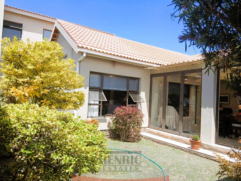 Rear view of the property featuring a well-maintained garden, tiled roof, and large aluminium sliding doors providing access to the interior living space.