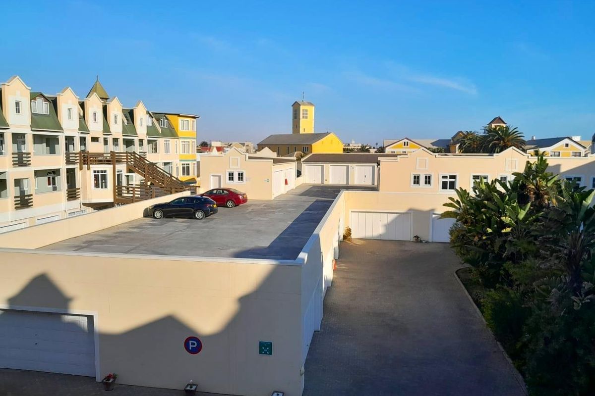 An elevated view of the apartment complex courtyard, featuring paved parking areas, multiple garage units, and surrounding residential building facades.