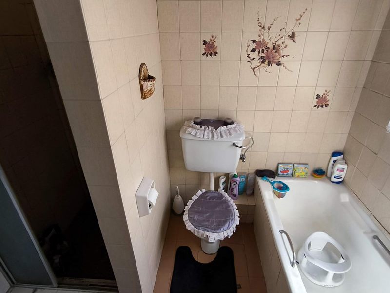 A functional bathroom featuring a standard bathtub, toilet, and shower enclosure with dated ceramic wall tiling.