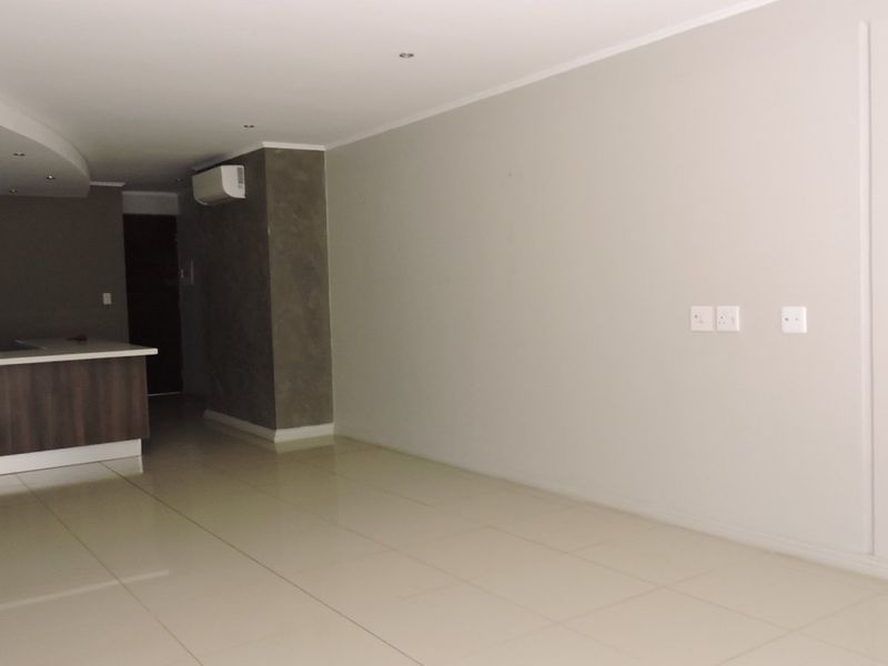 An open-plan living and kitchen area featuring neutral tiled flooring, recessed lighting, and a modern kitchen island with a breakfast counter.