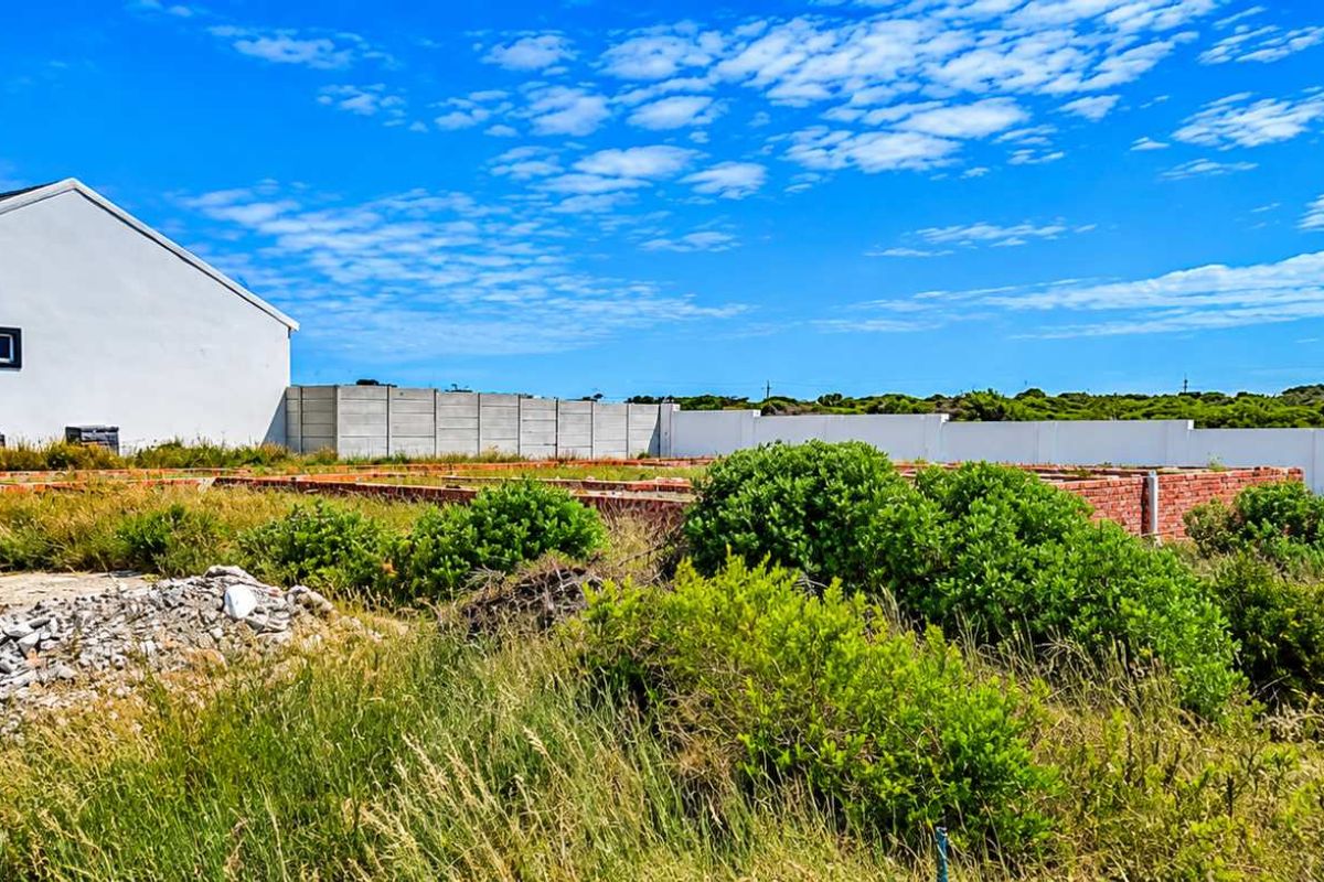 A vacant residential plot featuring an unfinished brick foundation, precast boundary walls, and overgrown vegetation, offering potential for future development.