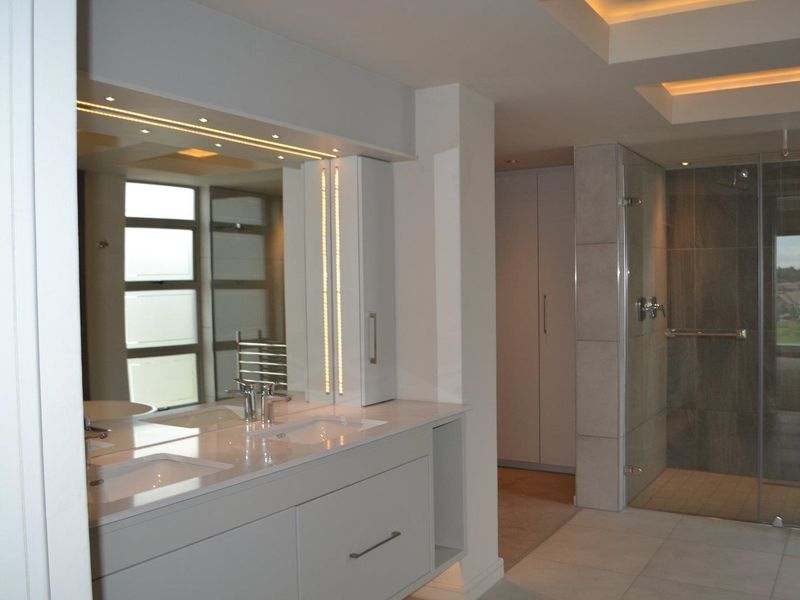 Modern bathroom featuring a double vanity with integrated lighting, a spacious walk-in shower with glass enclosure, and sleek built-in cabinetry.