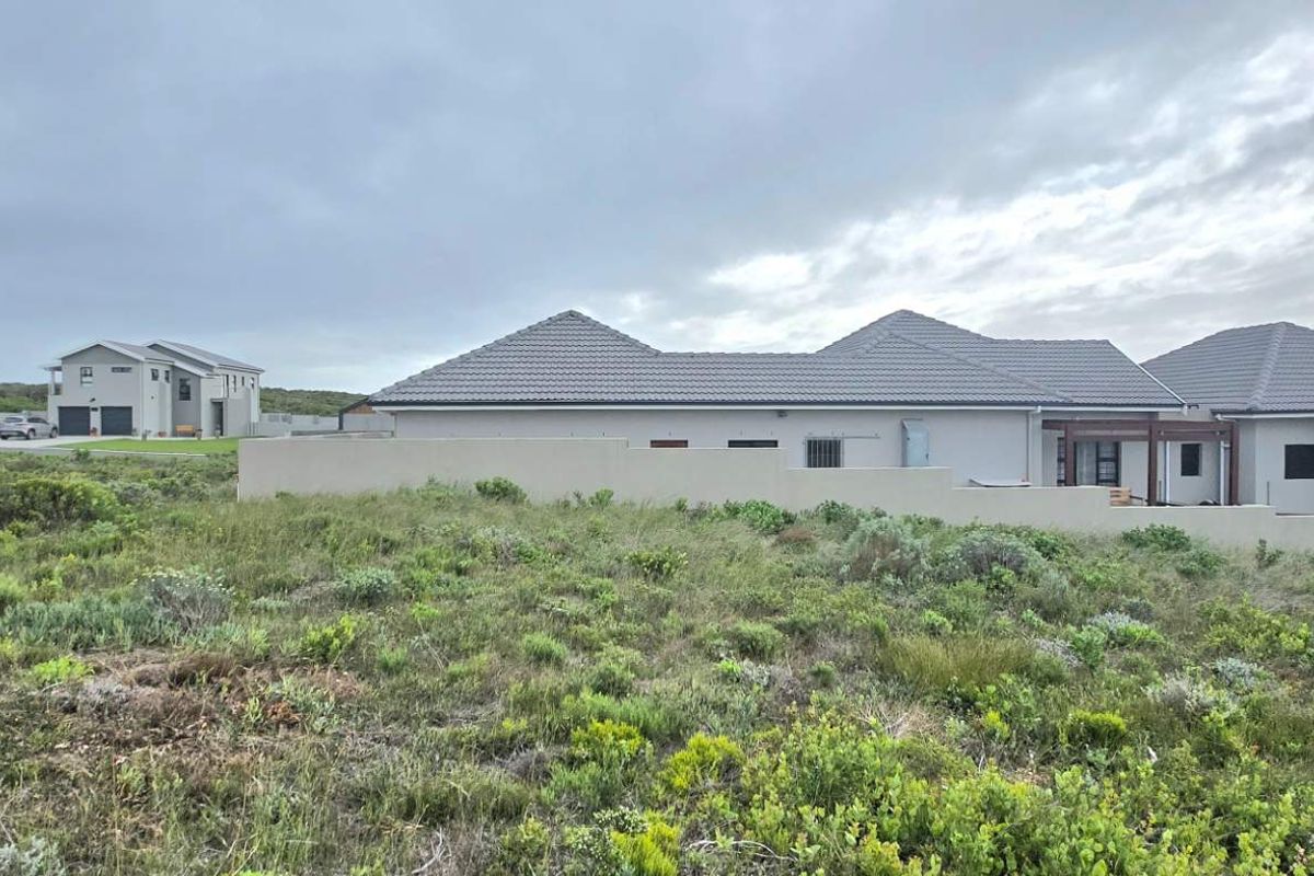 A view of a vacant residential plot featuring natural coastal vegetation with neighboring modern homes visible in the background.