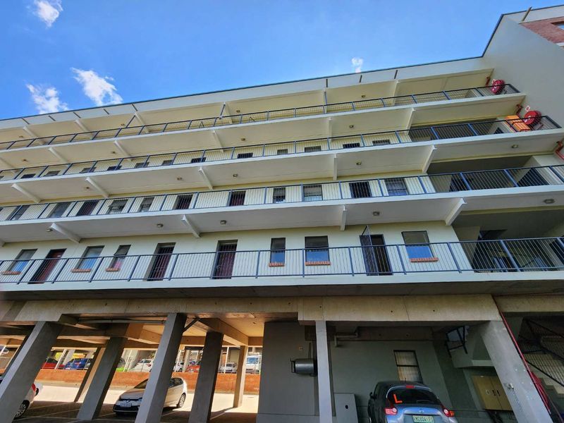 Low-angle view of a multi-story apartment building facade featuring stacked balconies with metal railings and a ground-level covered parking area.