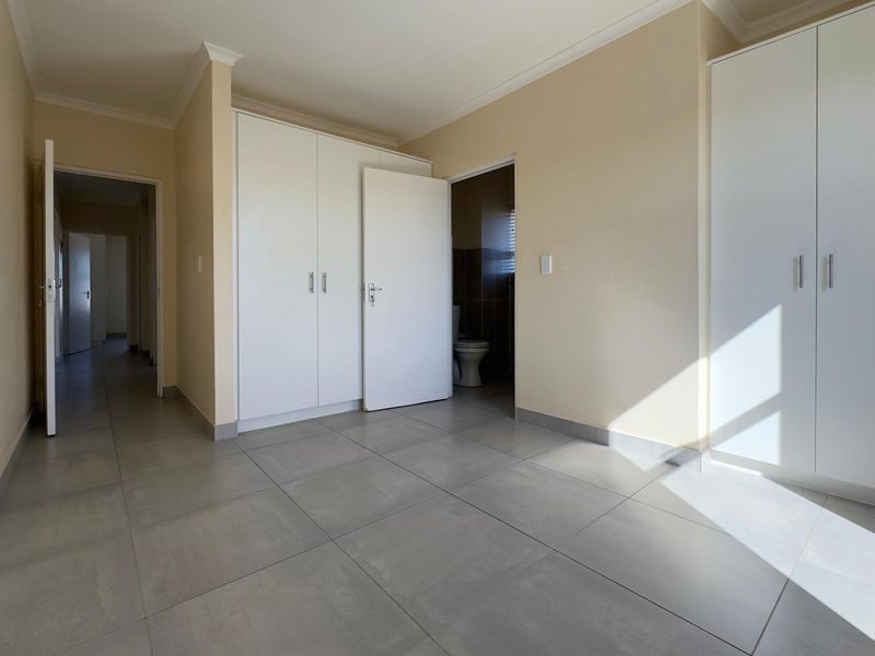 A bright, empty bedroom featuring neutral tiled flooring, built-in cupboards, and direct access to an en-suite bathroom.