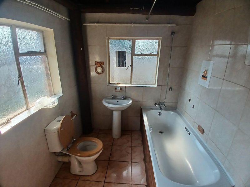 A dated bathroom featuring a pedestal basin, bathtub, and tiled finishes, offering a functional layout ready for modernization and cosmetic updates.