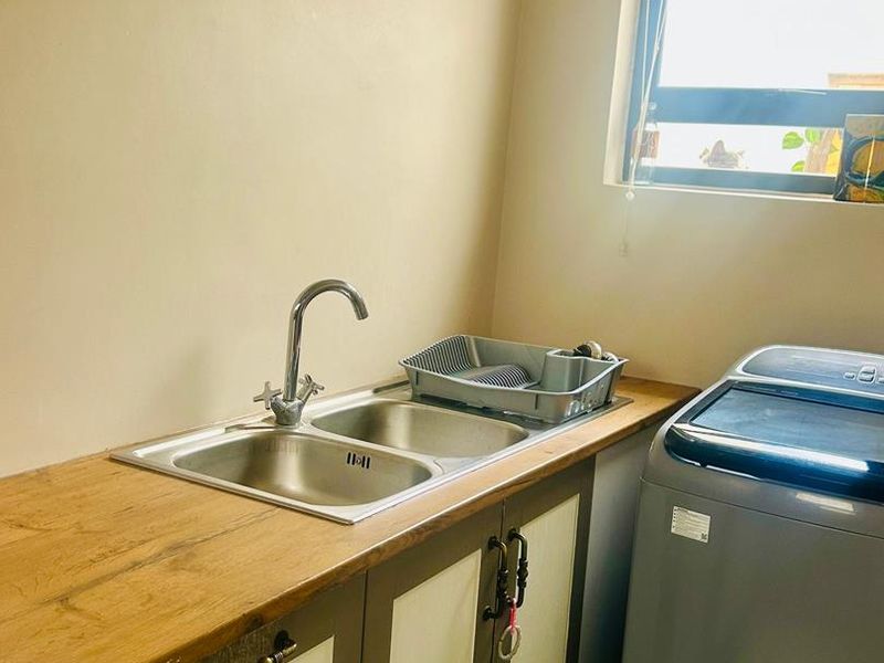 A functional laundry area featuring a stainless steel double sink, wooden countertop, and built-in cabinetry with space for a washing machine.