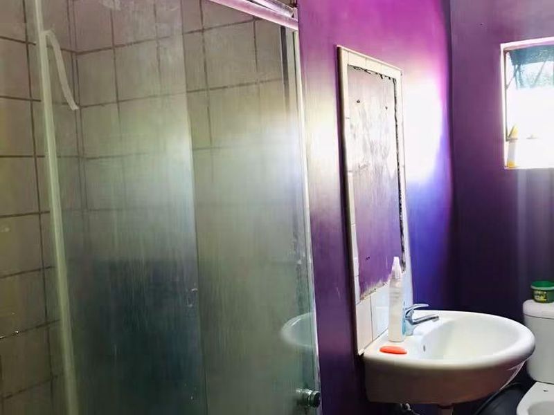 A compact bathroom featuring a shower enclosure, wall-mounted basin, and toilet, requiring cosmetic updates to improve the overall aesthetic and finish.