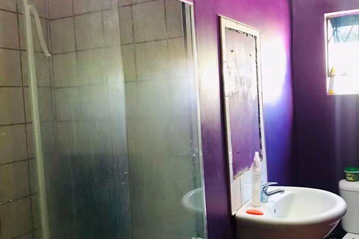 A compact bathroom featuring a shower enclosure, wall-mounted basin, and toilet, requiring cosmetic updates to improve the overall aesthetic and finish.