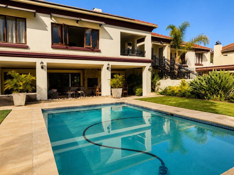 A well-maintained backyard featuring a swimming pool, covered patio area with a built-in fireplace, and an external staircase leading to the upper level.