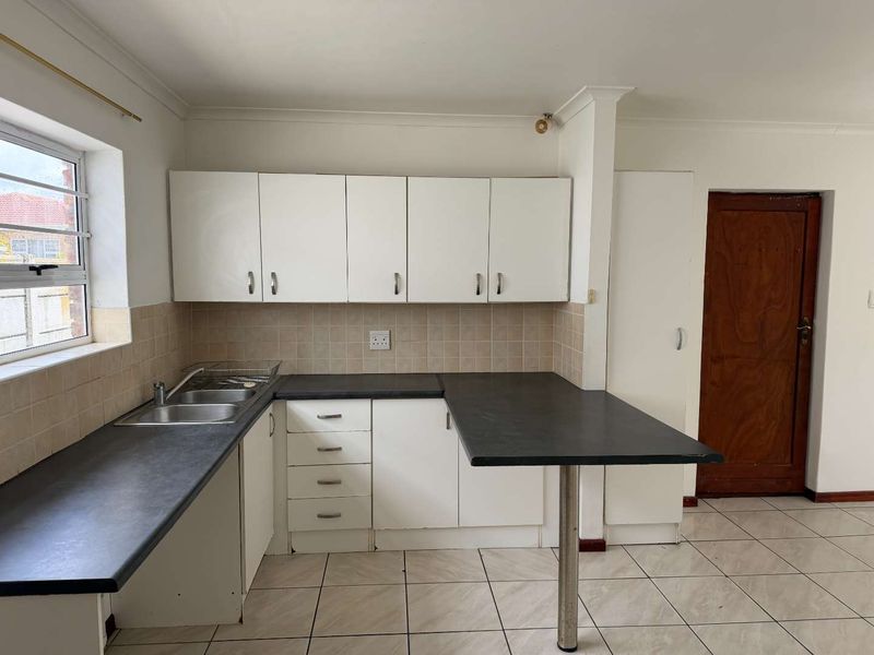 A functional kitchen featuring white cabinetry, dark laminate countertops, a breakfast bar, and tiled flooring, offering a clean canvas for potential modern updates.
