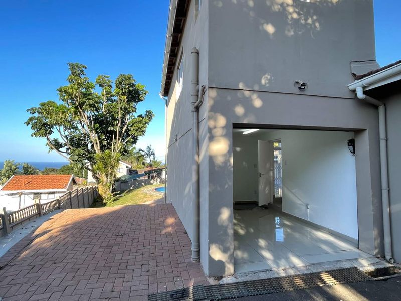A view of the garage exterior and paved driveway, featuring tiled flooring inside and a clear view of the surrounding neighborhood.