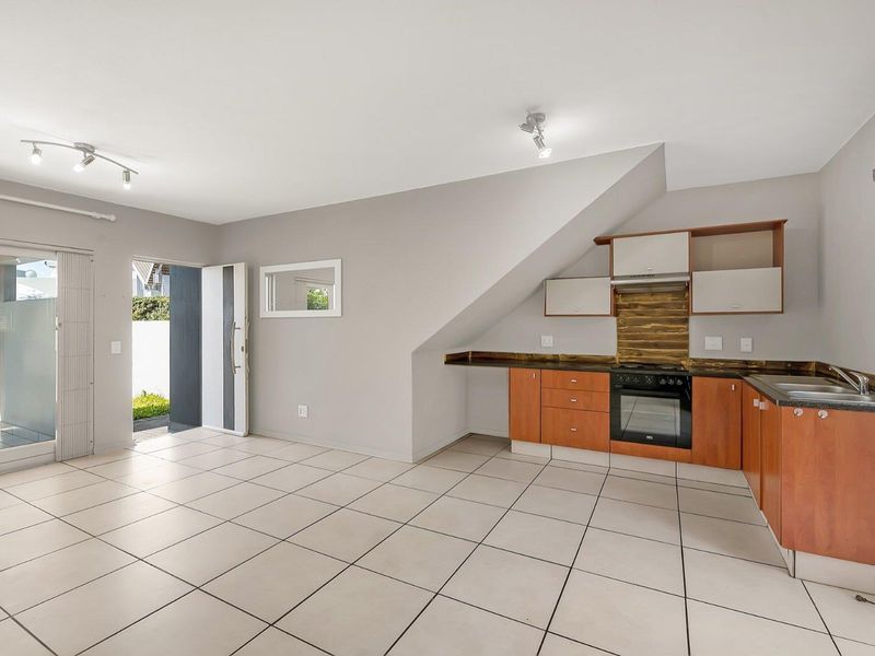 Open-plan living area featuring a compact kitchen with built-in cabinetry, oven, hob, and direct access to an outdoor patio area.