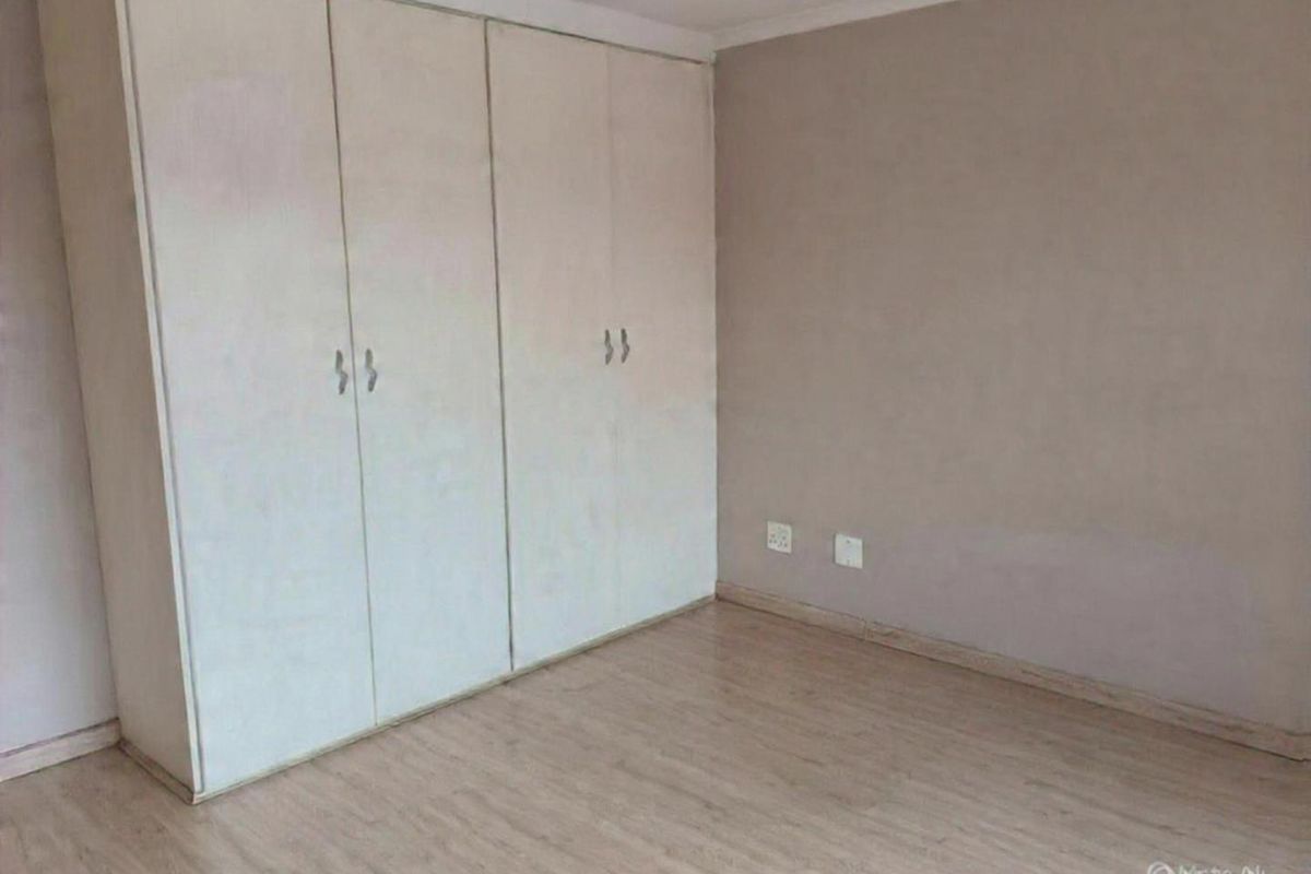 A bedroom featuring built-in cupboards and light-toned laminate flooring, offering a neutral canvas for personalization.