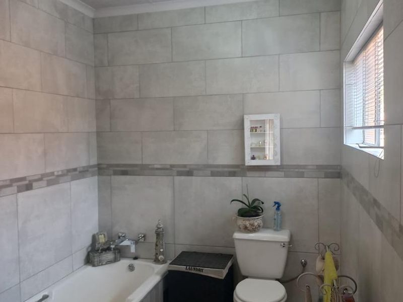 A functional bathroom featuring neutral wall tiling, a standard bathtub, and a toilet, illuminated by a central ceiling light fixture.