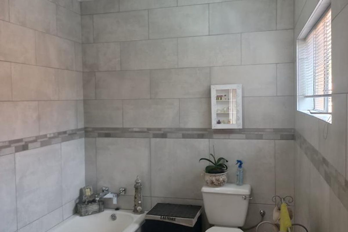 A functional bathroom featuring neutral wall tiling, a standard bathtub, and a toilet, illuminated by a central ceiling light fixture.