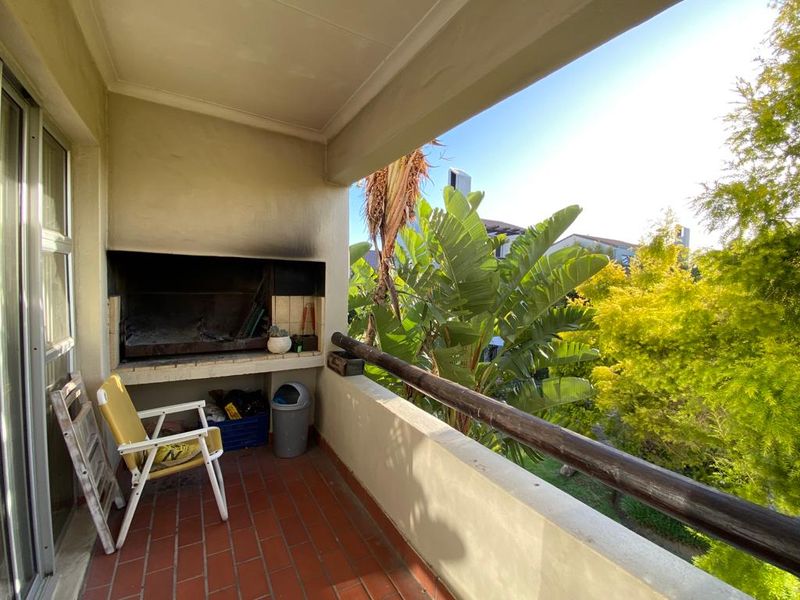 Covered balcony featuring a built-in braai, tiled flooring, and a railing, overlooking a lush garden area.