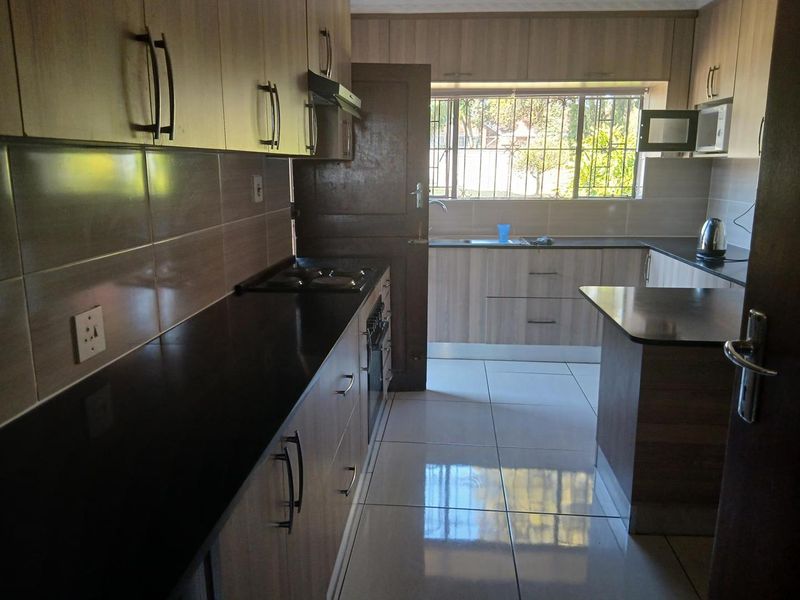 A functional kitchen featuring laminate cabinetry, dark granite countertops, built-in oven, hob, extractor fan, and tiled flooring with natural light.
