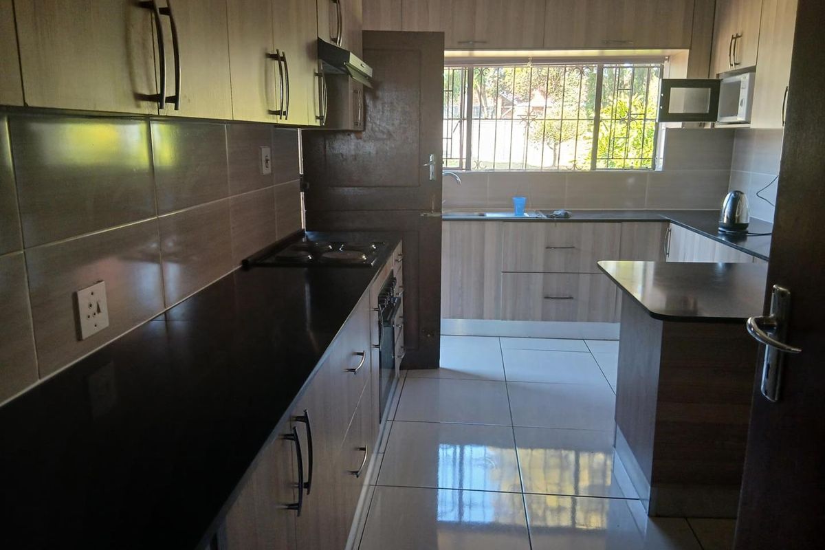 A functional kitchen featuring laminate cabinetry, dark granite countertops, built-in oven, hob, extractor fan, and tiled flooring with natural light.