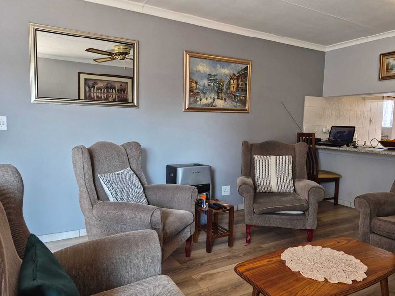 Open plan living area featuring laminate flooring, a ceiling fan, and a breakfast bar connecting to the kitchen space.