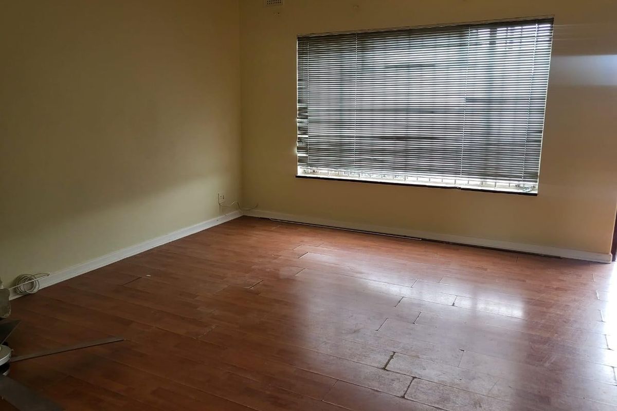 An empty living room featuring laminate flooring and large windows with venetian blinds, offering a blank canvas for potential renovation or interior design updates.