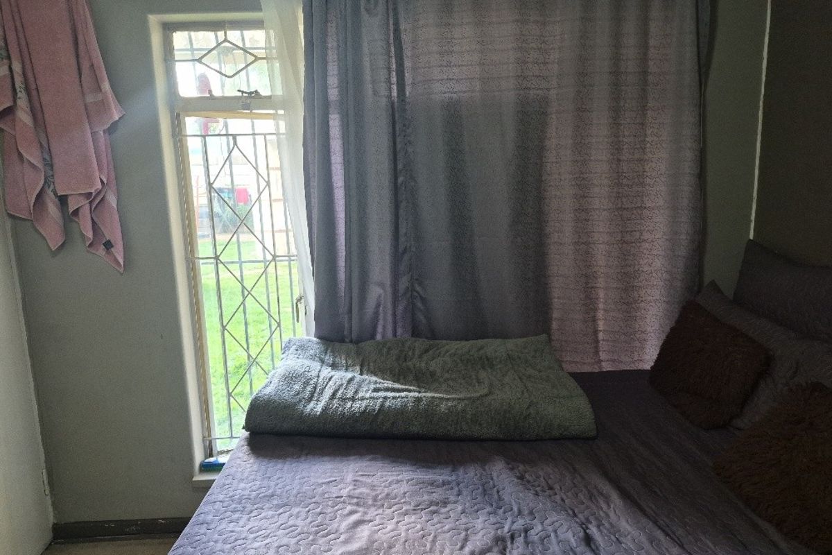 A bedroom featuring a window with a security gate and neutral wall finishes.