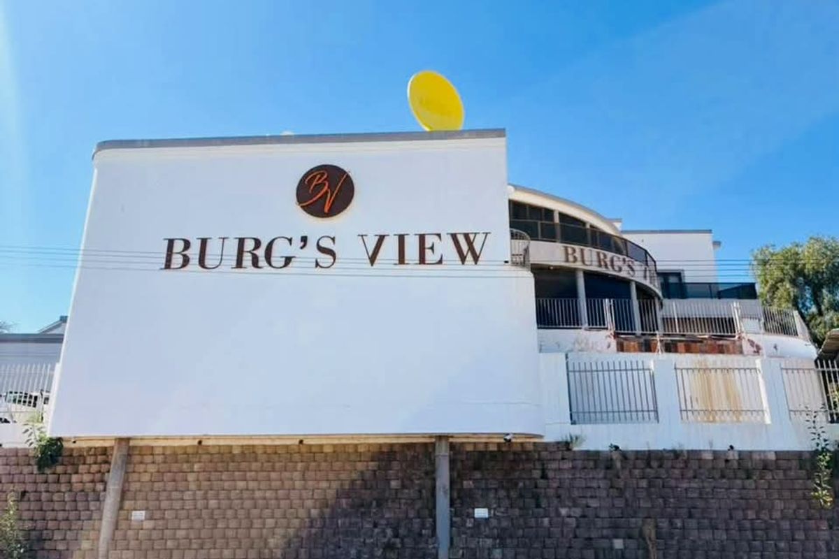 Exterior view of the hotel building featuring a prominent signage wall, metal security fencing, and a raised balcony area.