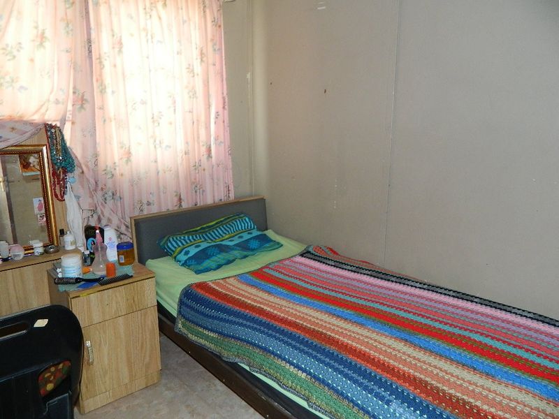 A compact bedroom featuring a window with floral curtains and plain wall finishes, offering a functional space for rest.