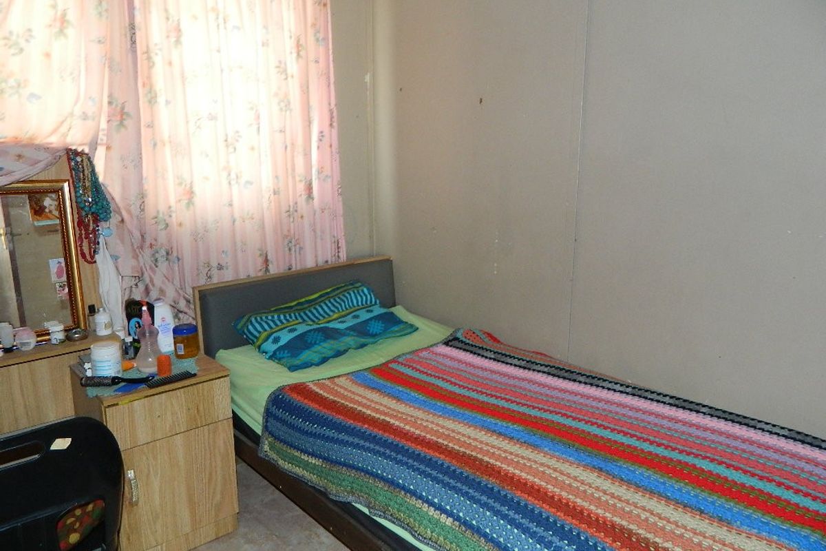A compact bedroom featuring a window with floral curtains and plain wall finishes, offering a functional space for rest.
