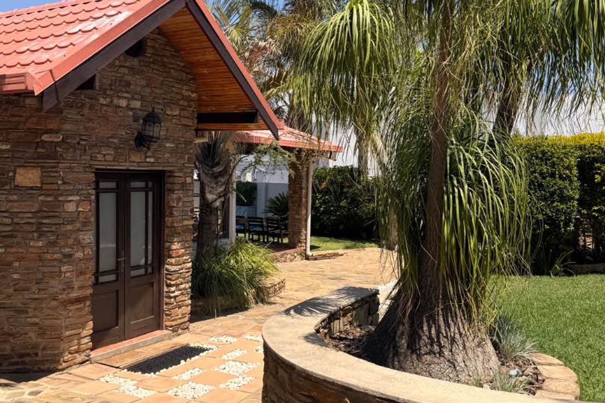 A well-maintained rear garden area featuring stone-clad exterior walls, a tiled roof structure, and a paved patio with a curved stone retaining wall.