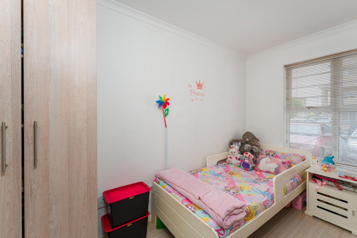 A bedroom featuring a built-in wardrobe with light wood-grain finish and a window fitted with venetian blinds.