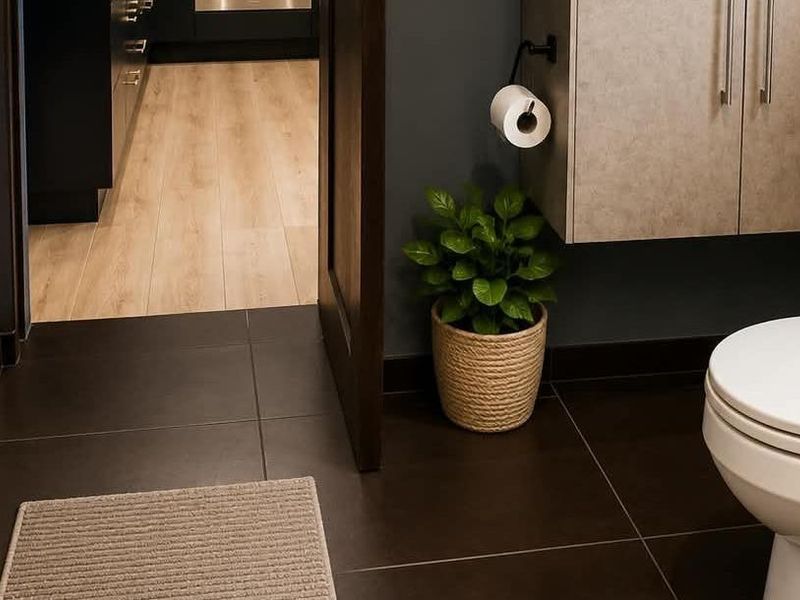 Modern bathroom featuring dark floor tiles, a wall-mounted vanity cabinet, and a clean white toilet, with a view into the adjacent living area.