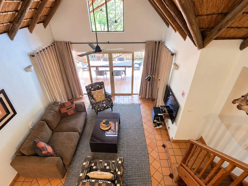 Spacious living area featuring a high vaulted thatched ceiling with exposed timber rafters, terracotta flooring, and direct access to an outdoor patio.