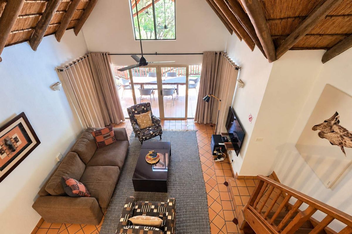 Spacious living area featuring a high vaulted thatched ceiling with exposed timber rafters, terracotta flooring, and direct access to an outdoor patio.