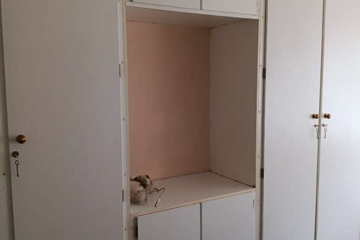 A bedroom featuring dated, built-in floor-to-ceiling cupboards with integrated shelving and storage compartments.