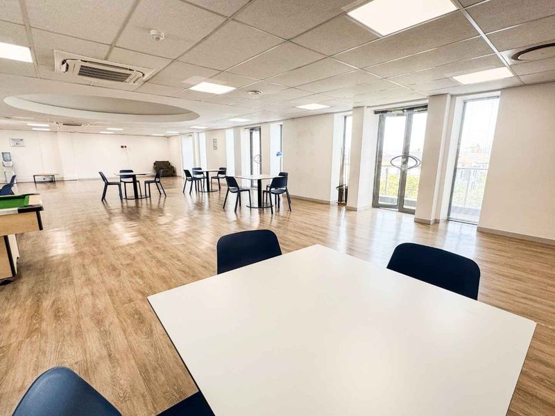 Spacious open-plan office or communal area featuring modern laminate flooring, suspended ceilings with recessed lighting, and large windows providing ample natural light.