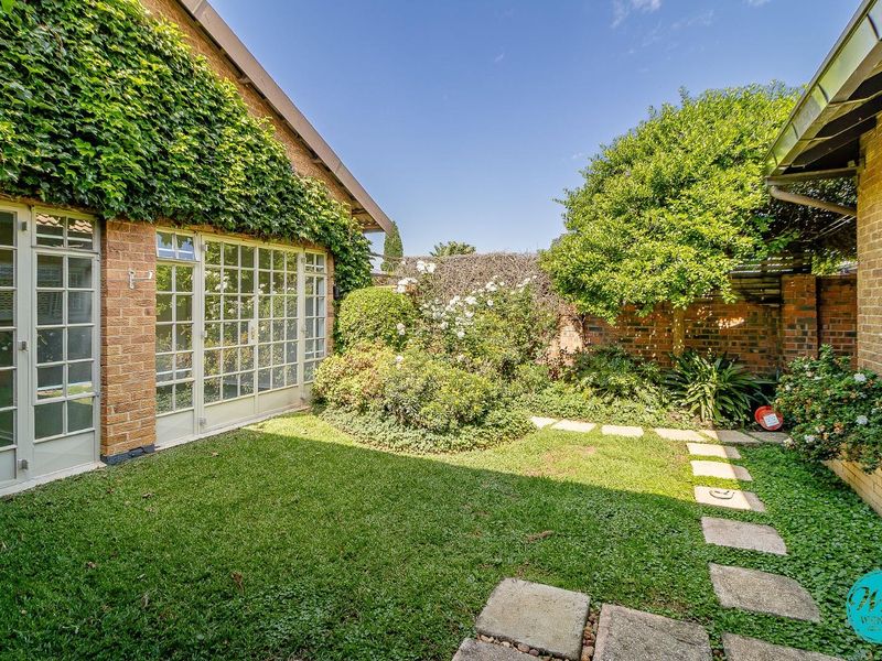 A private rear garden featuring a lush lawn, stone paver pathway, and classic brick facade with elegant french doors.
