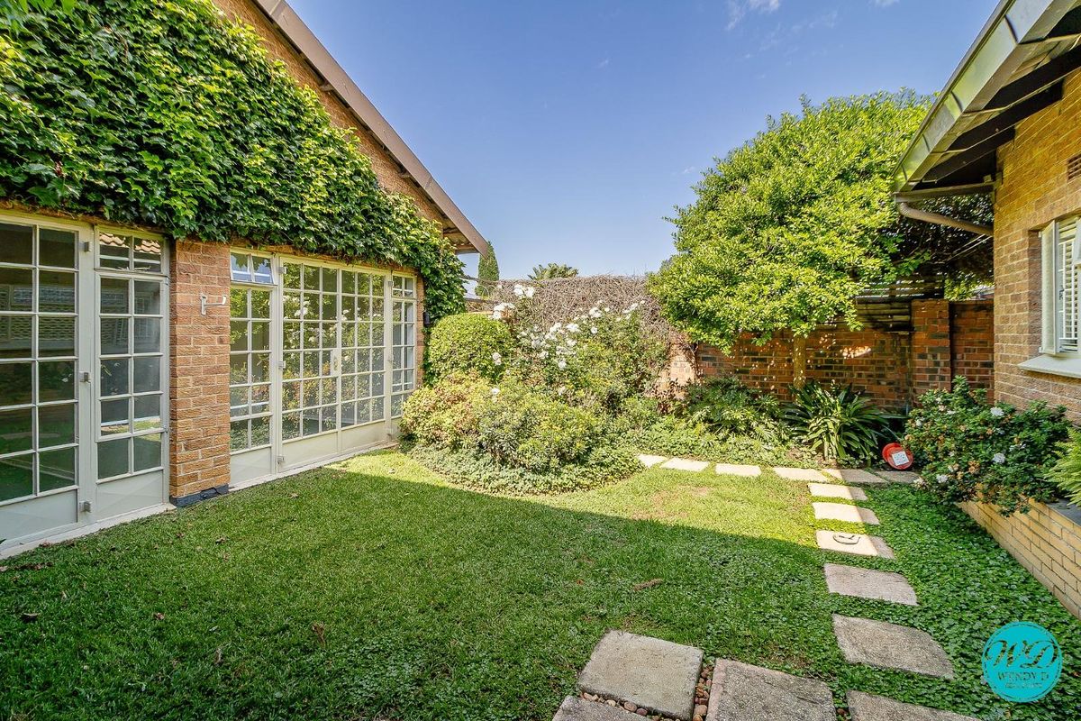 A private rear garden featuring a lush lawn, stone paver pathway, and classic brick facade with elegant french doors.