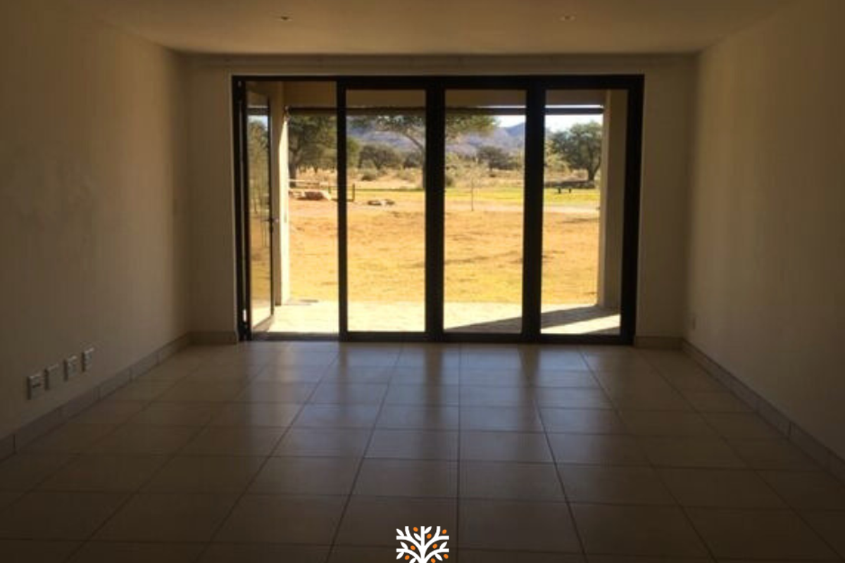 An empty living room featuring large sliding glass doors that open onto a patio, providing natural light and views of the surrounding landscape.