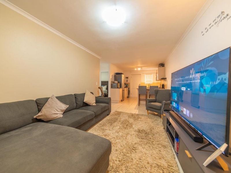 Open-plan living area featuring tiled flooring and a connected kitchen space with breakfast counter, providing a functional and integrated layout.