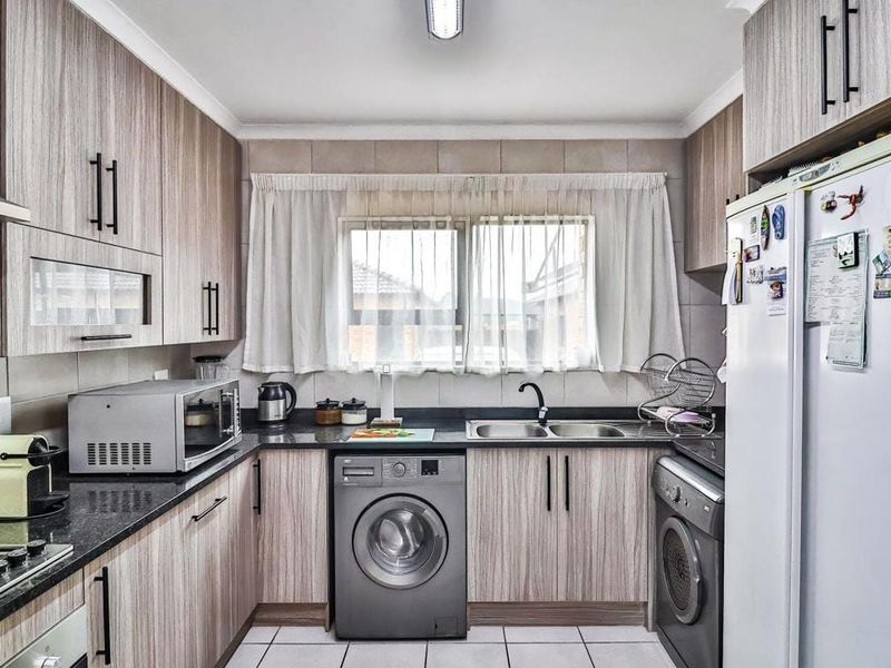 Functional kitchen featuring wood-look laminate cabinetry, granite countertops, a double basin sink, and integrated laundry appliance connections.