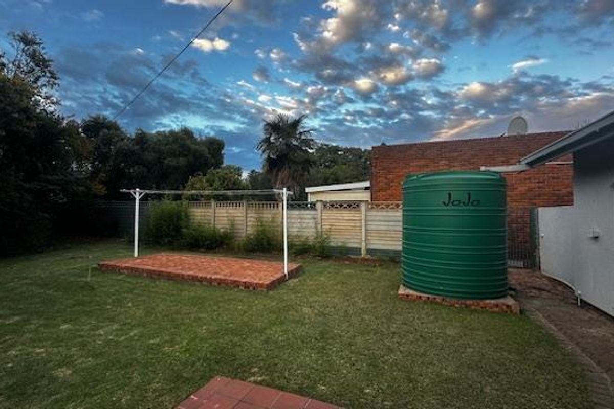 A spacious rear garden featuring a green water storage tank, a brick-paved area, and a metal clothesline set against a boundary wall.