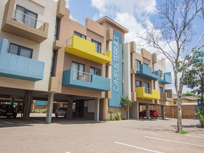 Exterior view of Campus Terrace apartment complex featuring modern multi-story architecture with colorful balconies and convenient covered ground-level parking.