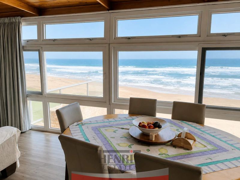 A bright dining area featuring expansive windows with direct, unobstructed views of the ocean and sandy beach.