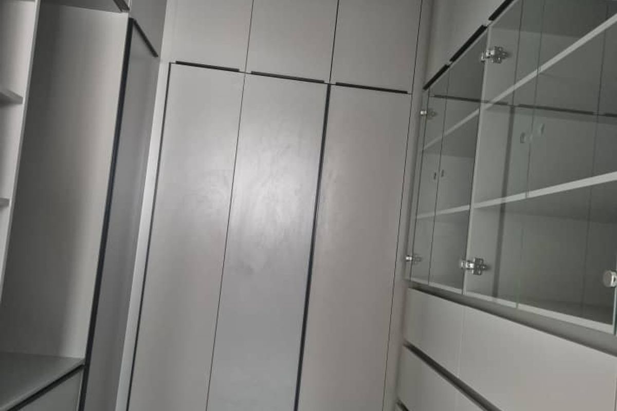 A modern walk-in closet or dressing area featuring extensive built-in cabinetry, glass-fronted storage, and sleek tiled flooring.