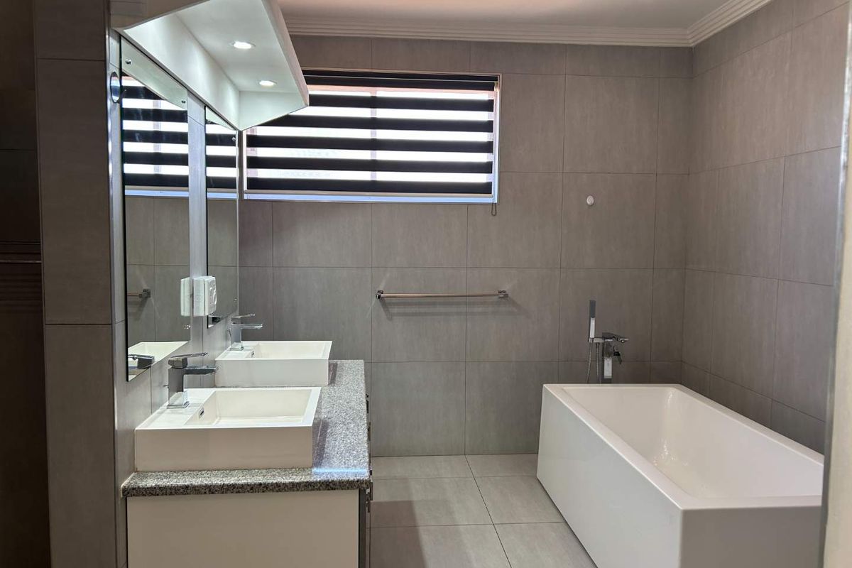 Modern bathroom featuring a double vanity with stone countertop, integrated sinks, and a contemporary freestanding bathtub with wall-tiled finishes.