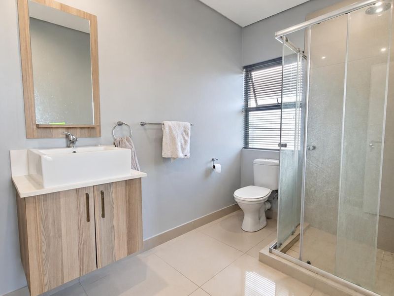 Modern bathroom featuring a wood-finish vanity with a vessel sink, a glass-enclosed shower, and neutral tiled flooring.
