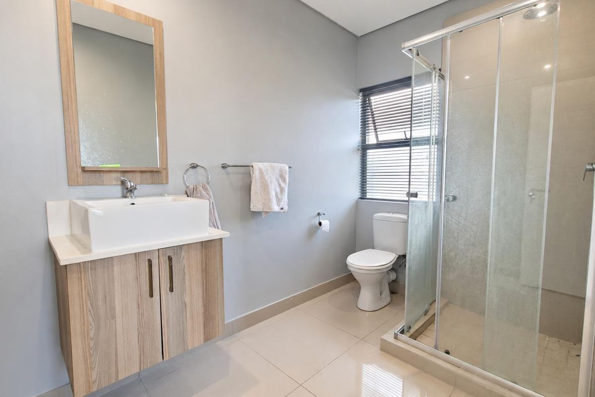 Modern bathroom featuring a wood-finish vanity with a vessel sink, a glass-enclosed shower, and neutral tiled flooring.